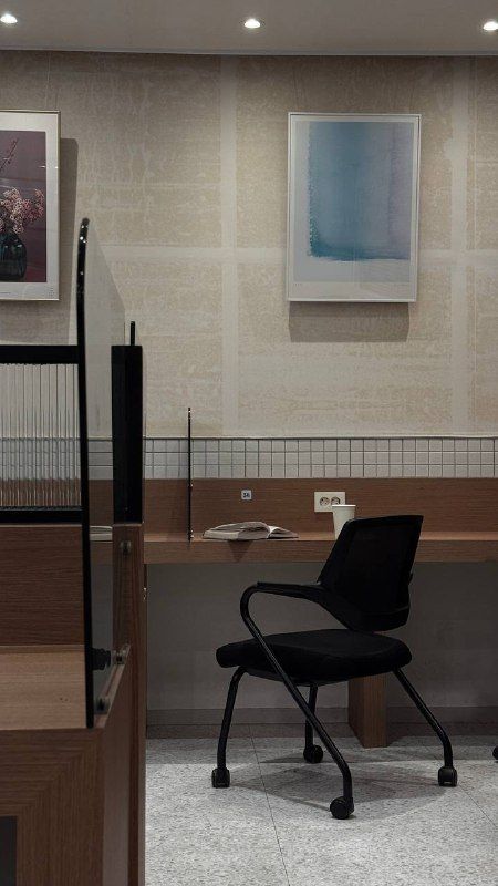 An empty office chair and desk beneath framed paintings