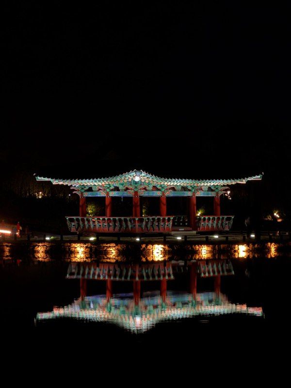 A palace pavilion lit at night, mirrored perfectly in black water