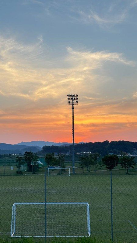 Sunset glowing over a sports field and floodlight tower