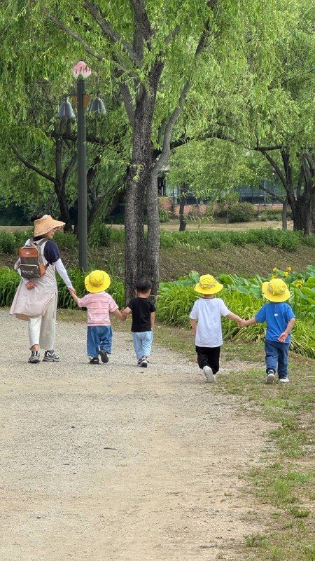 A parent and small children in yellow hats walking along a leafy path