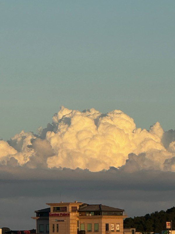 A towering white cumulus cloud above a low building