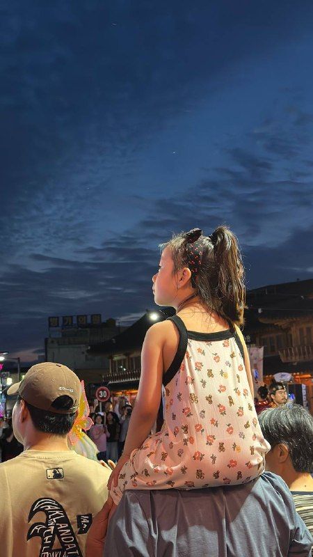 A girl on her father's shoulders at a night festival