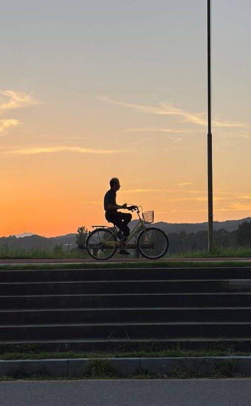 A cyclist silhouetted on a riverside dyke against an orange evening sky