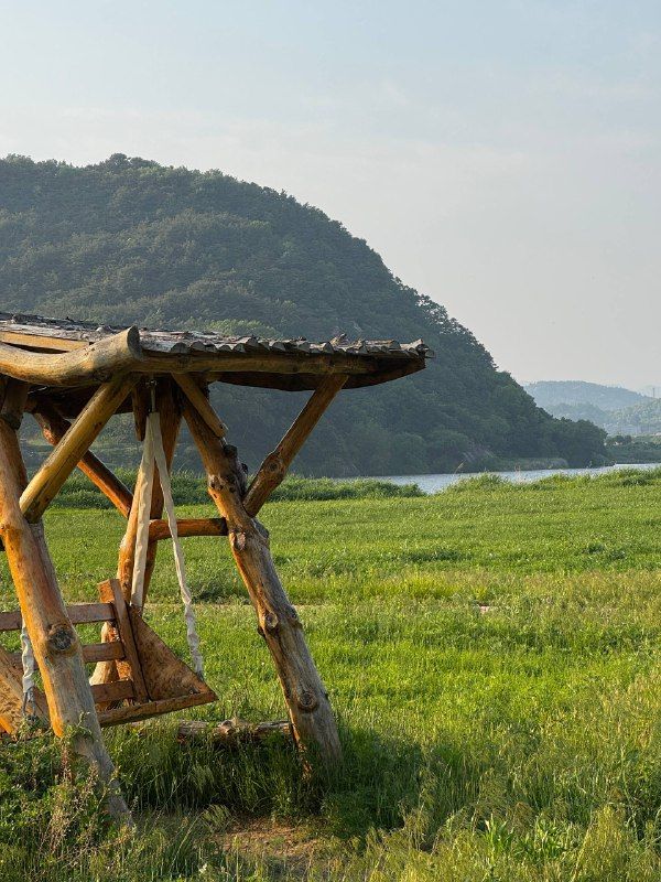 A rustic wooden swing frame in a green meadow below a mountain