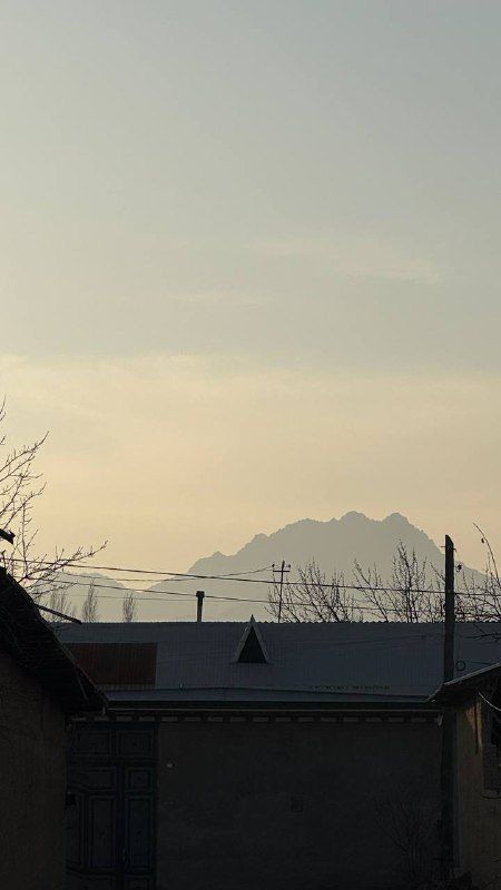 A pale evening sky over dark rooftops and a mountain ridge