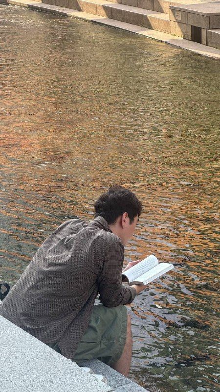 A man reading a book by the edge of a city stream