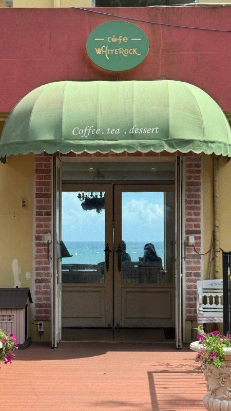 A café entrance under a green awning with glass double doors