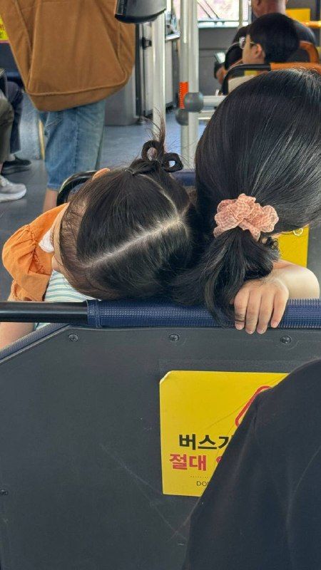 A child asleep on a parent's shoulder on a bus