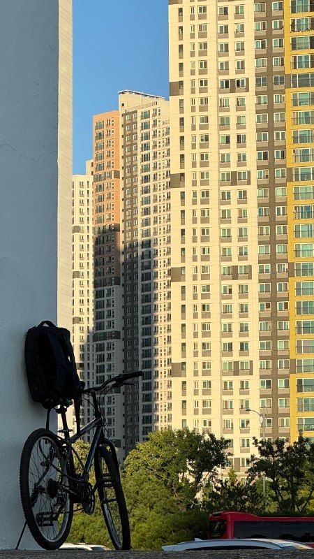 A bicycle parked beside a tall apartment block in sunlight