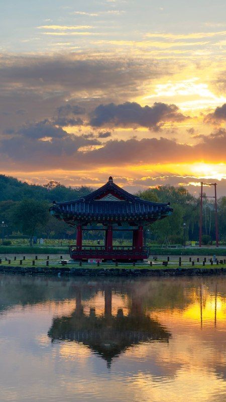 A red pavilion mirrored in still water under a gold sunrise