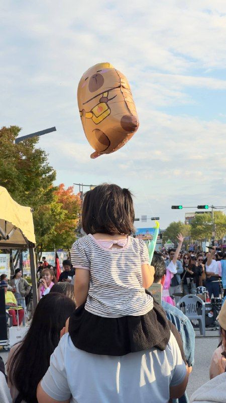 A small girl on her father's shoulders watching a balloon parade at an autumn festival