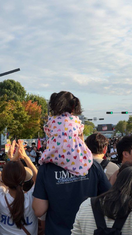A girl in a flowered jacket on her father's shoulders in a festival crowd