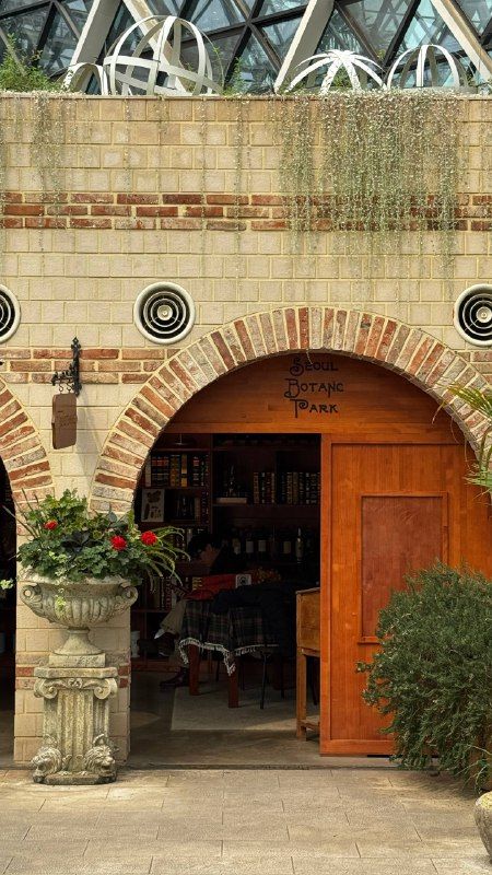 A brick archway and red doors inside a glass greenhouse