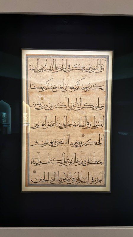 A framed page of Qur'anic calligraphy in a dark museum gallery
