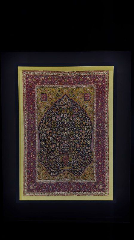 An ornate carpet lit in a darkened museum room